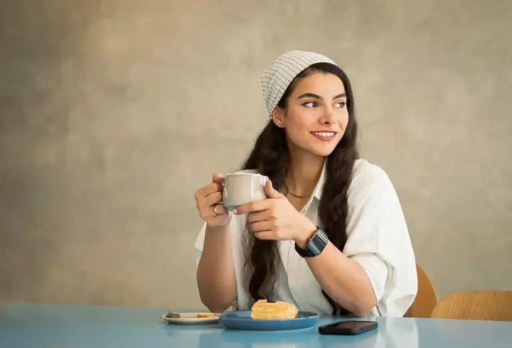 Una mujer con un café y el celular en la mesa